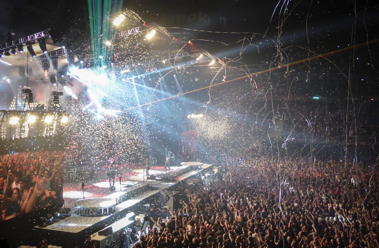 Vibrant concert scene with dynamic lighting, confetti, and a large enthusiastic crowd.